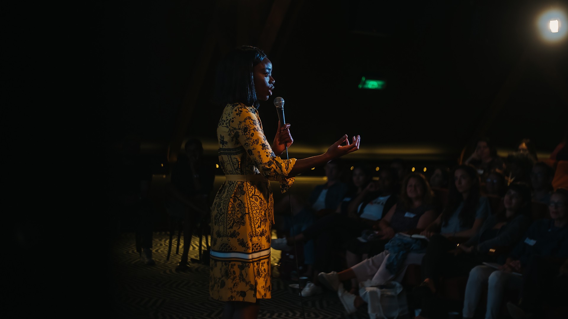 Speaker in a yellow patterned dress addresses an audience with a microphone, event coverage by a professional photographer in Amsterdam