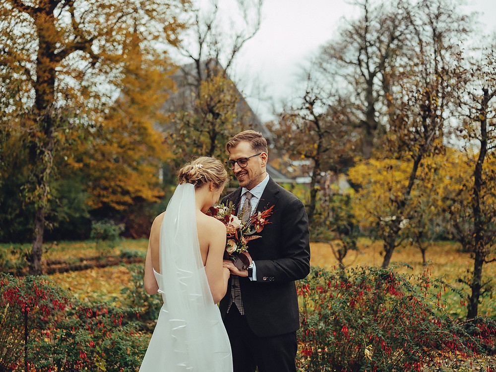 Bruidspaar deelt een stil moment tussen herfstbladeren, haar boeket in roest- en crèmetinten, een trouwfotoshoot in Amsterdam