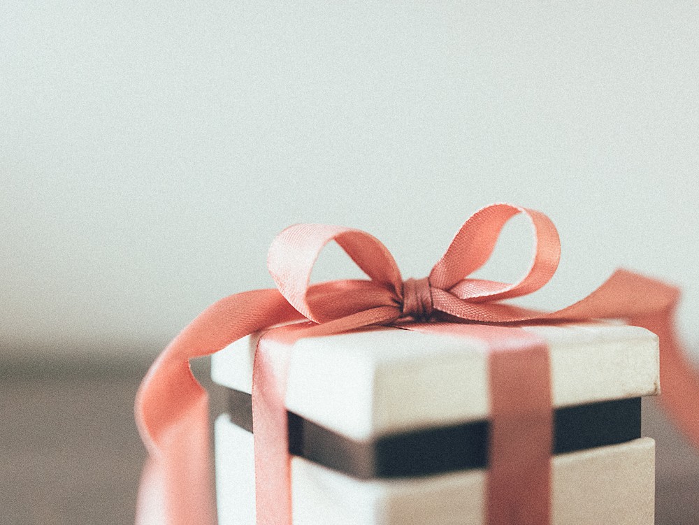 White gift box tied with a soft pink satin ribbon and a large bow, standing against a light gray background