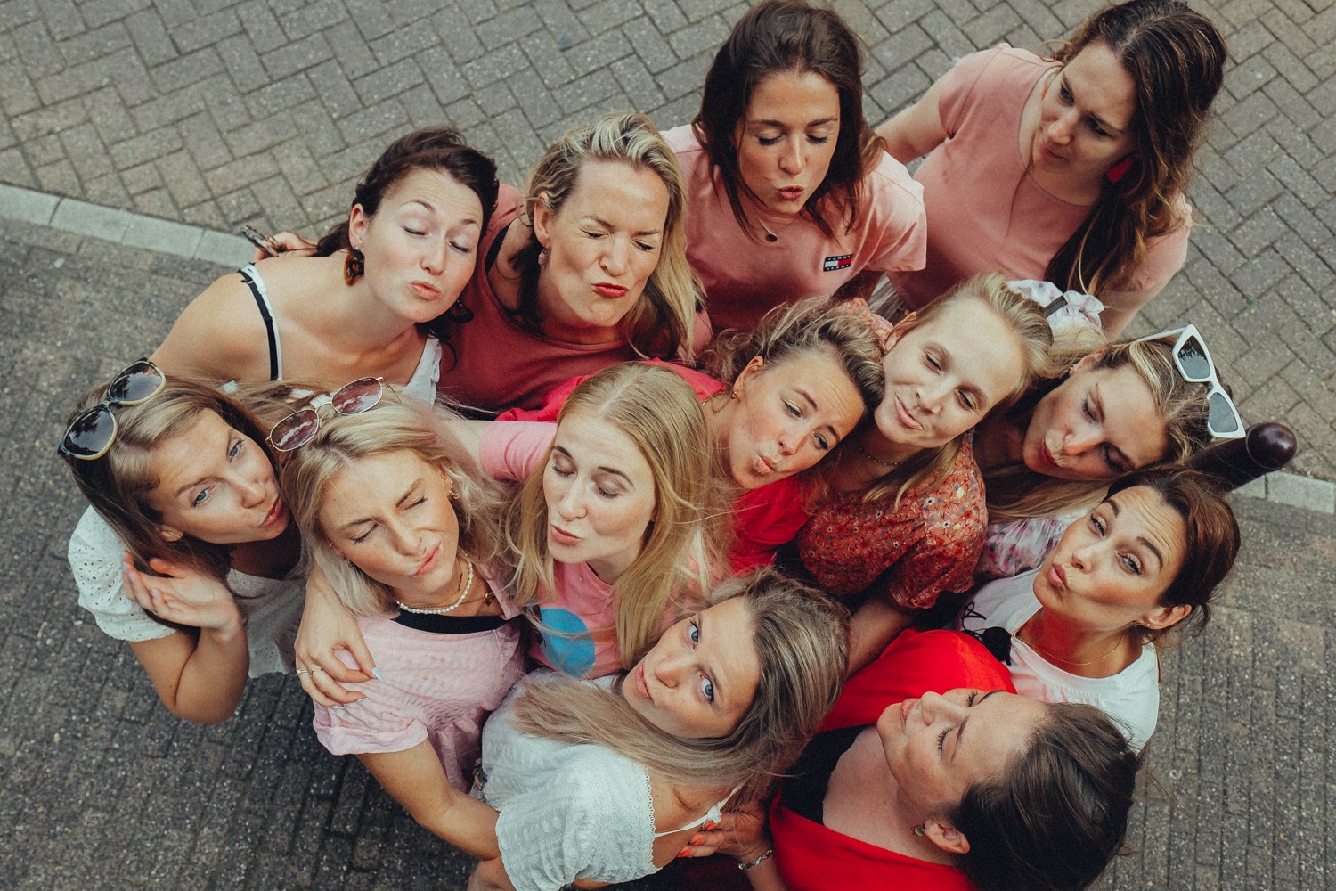 Circle of friends pouting kisses up at the camera, seen from above, pink and red tops and sunglasses in their hair