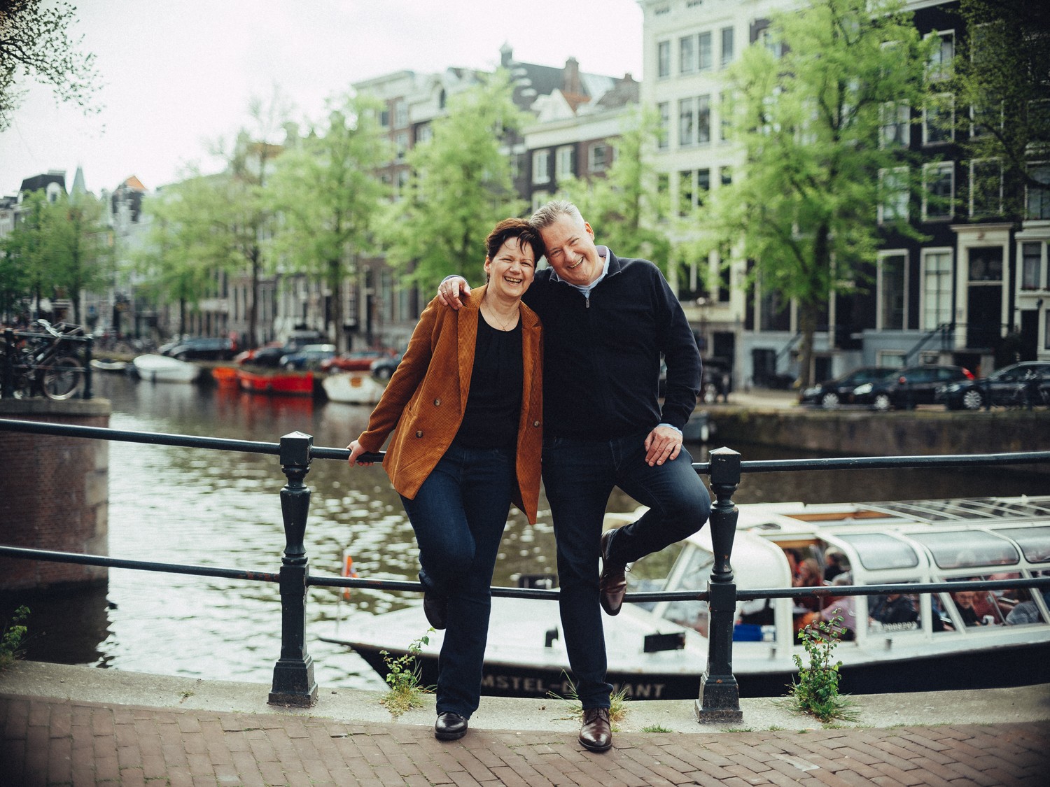 Ouders zitten samen op de leuning van de gracht op hun trouwdag, met aangemeerde rondvaartboten erachter