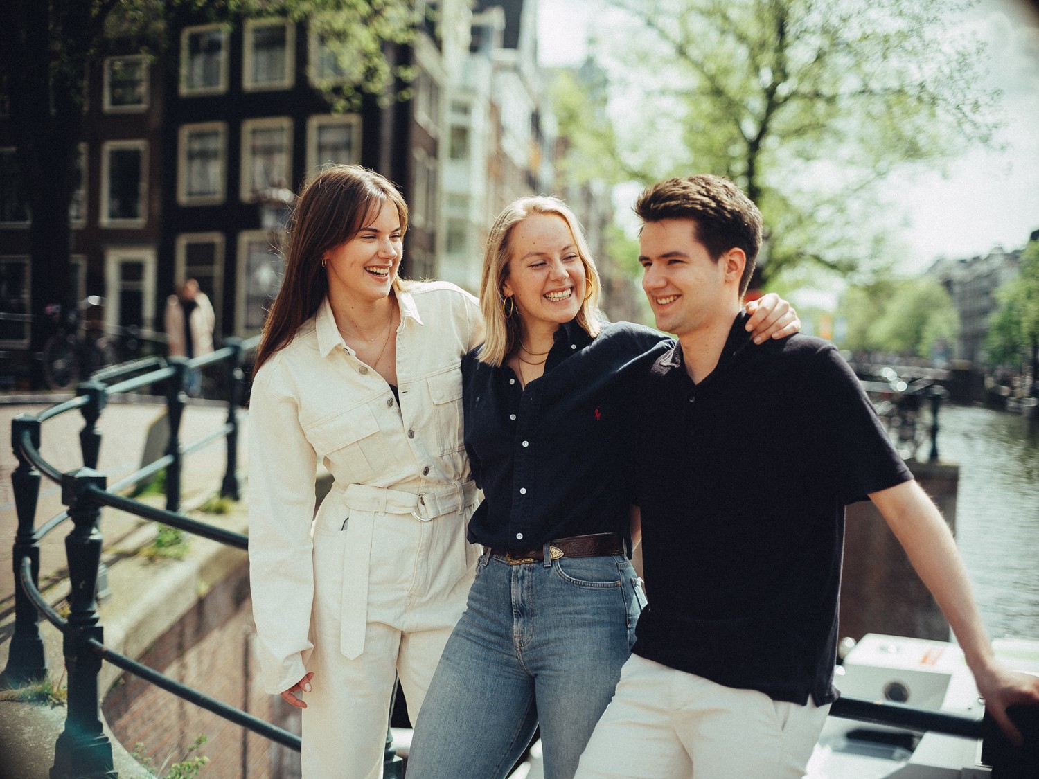 Drie volwassen kinderen lachen arm in arm langs de gracht, op een middag die een cadeau was voor de trouwdag van hun ouders