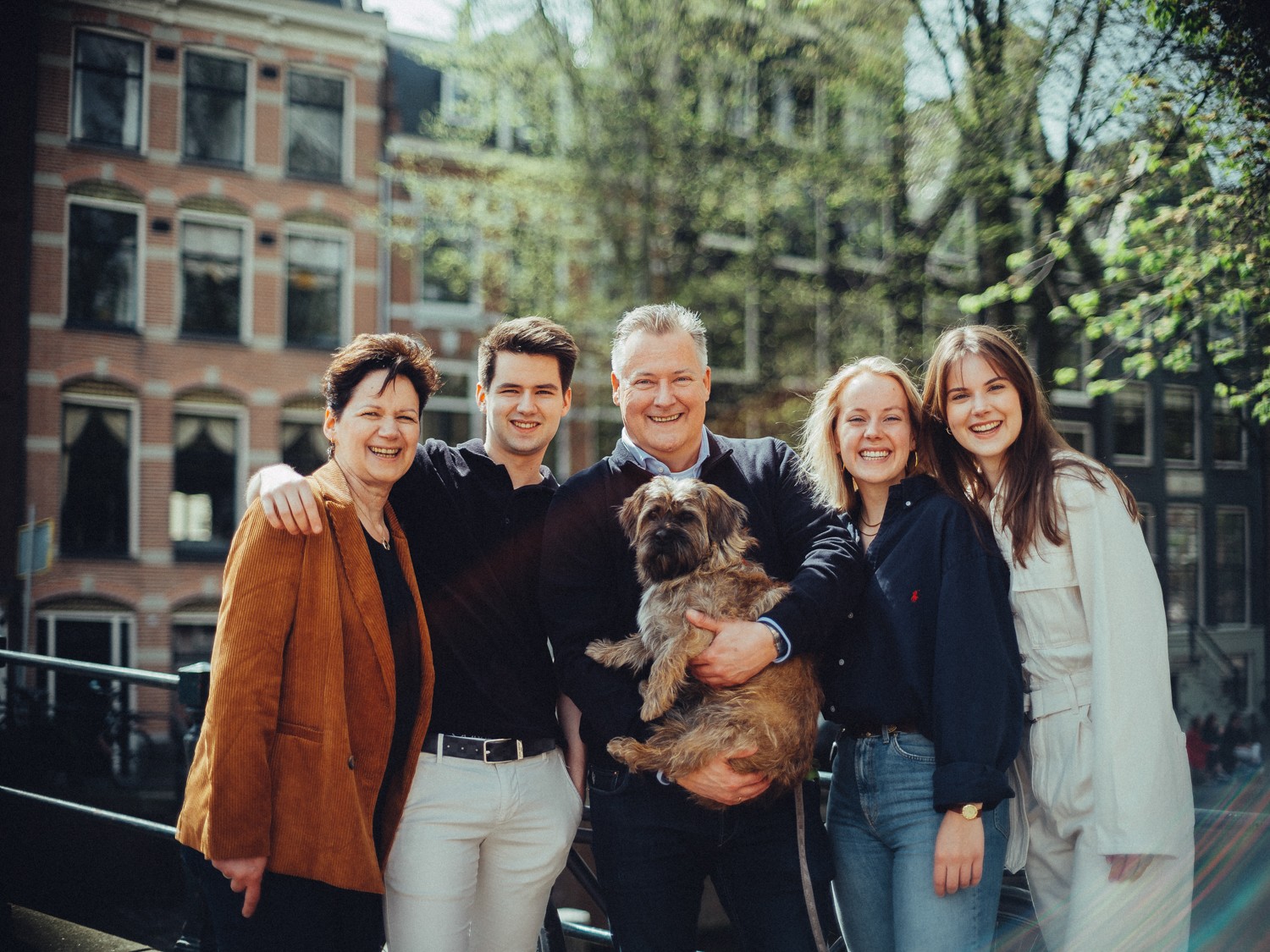 Gezin in een stevige groepsknuffel, lachend tijdens een wandeling als cadeau voor de trouwdag, de vader met de hond in de zon