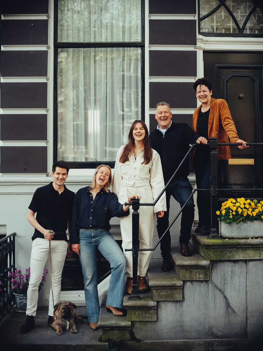 Gezin op de stoep van een grachtenpand bij gele bloemen na hun wandeling op de trouwdag, de terriër op de onderste trede