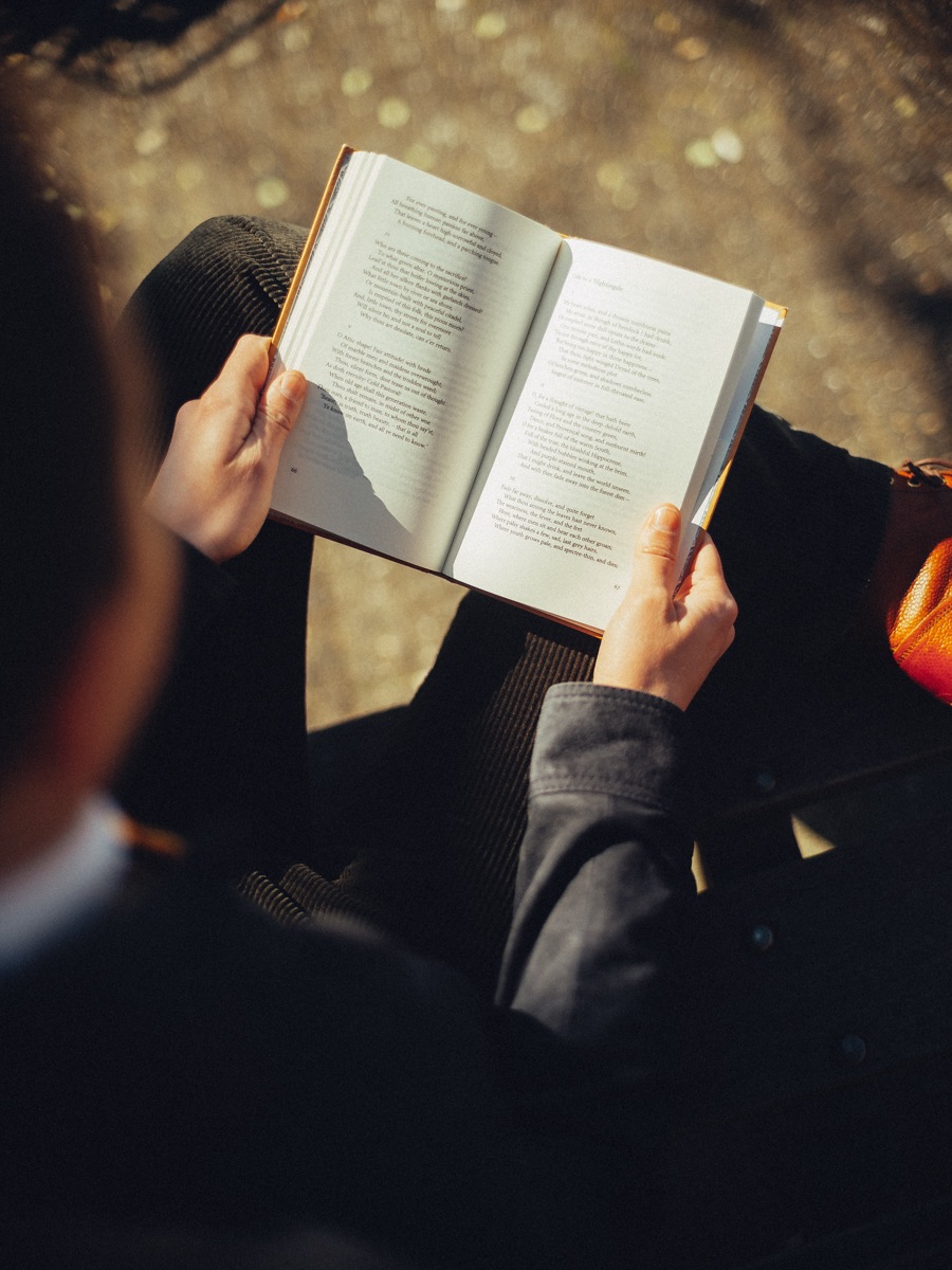 Handen met een open boek van achteren gezien, de bladzijden fel in de zon tegen een zachte bruine achtergrond