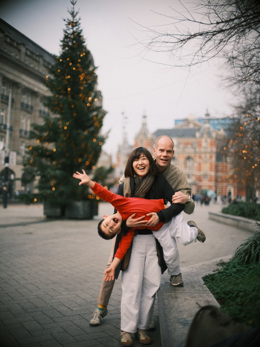 Joyful parents holding their son in a red sweater near a lit Christmas tree while enjoying fun things to do in Amsterdam with kids in winter