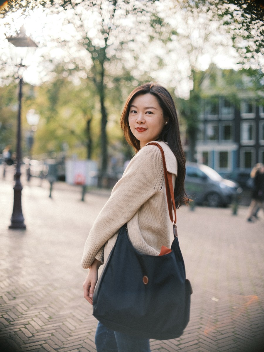 Vrouw kijkt over haar schouder om met een donkerblauwe canvas tas voor zich, de bomen gloeien in de herfstzon