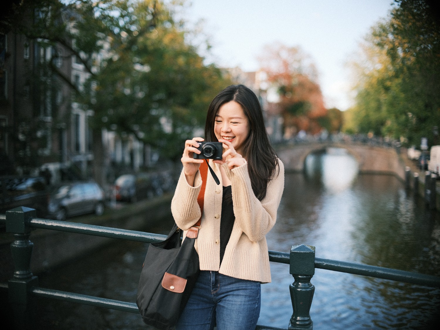 Soloreiziger in Amsterdam lacht terwijl ze de gracht in beeld brengt met haar camera op het hek, met een brug in de verte