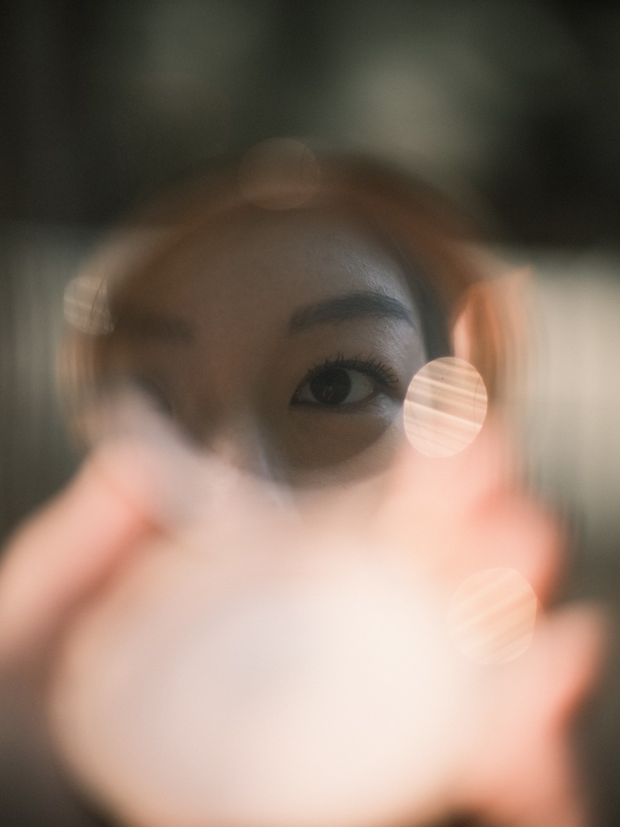 Eén donker oog weerspiegeld in een rond zakspiegeltje, met warme lichtvlekjes rond de rand van het glas in het late licht