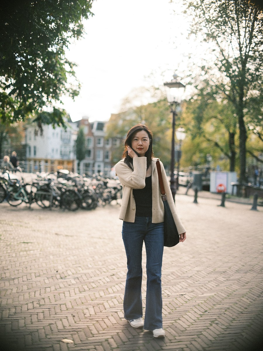 Soloreiziger staat in een straat met klinkers in Amsterdam met een hand in haar haar, met fietsen en een ijzeren lantaarnpaal erachter