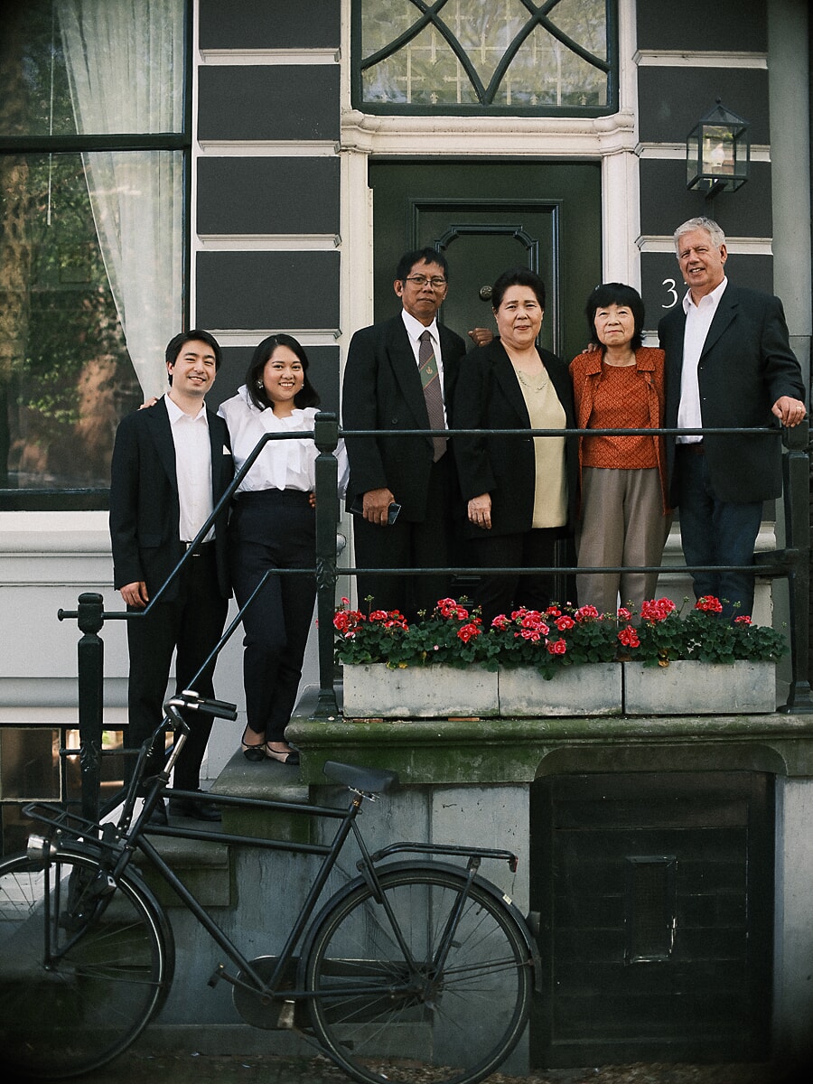 Three generations in formal dress on the geranium-lined steps of an Amsterdam canal house