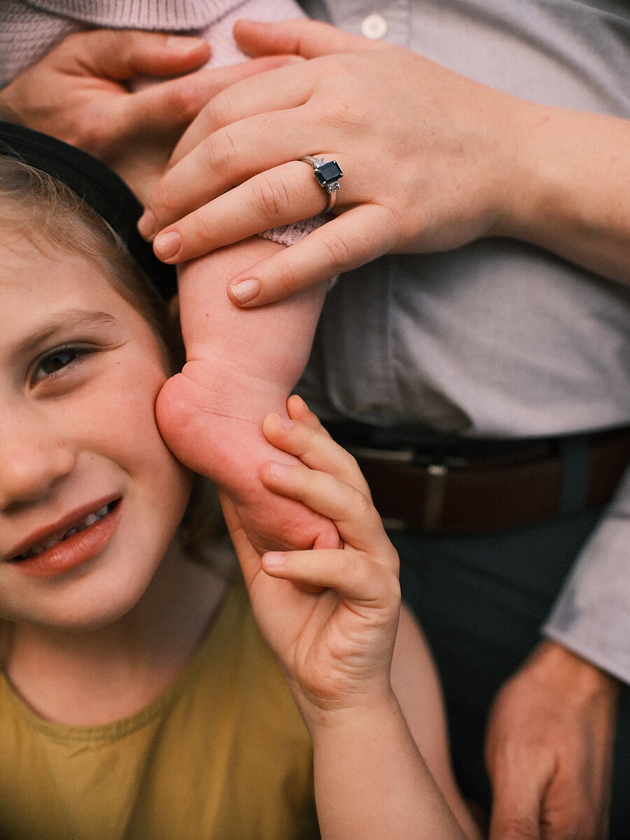 Close-up of a child's smile as her parents' hands rest against her cheek, a detail from a family photoshoot