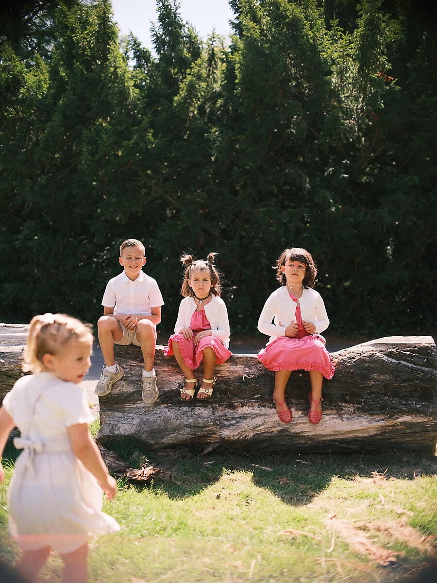Four children in matching pink along a fallen log during a family photoshoot in an Amsterdam park