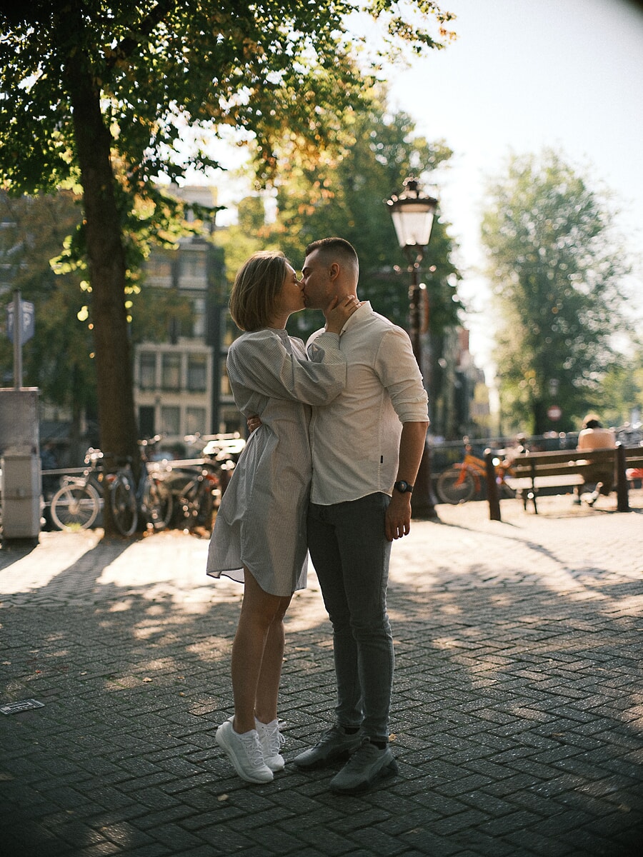 Engaged couple kissing on a sunlit square during an outdoor couple photoshoot in Amsterdam