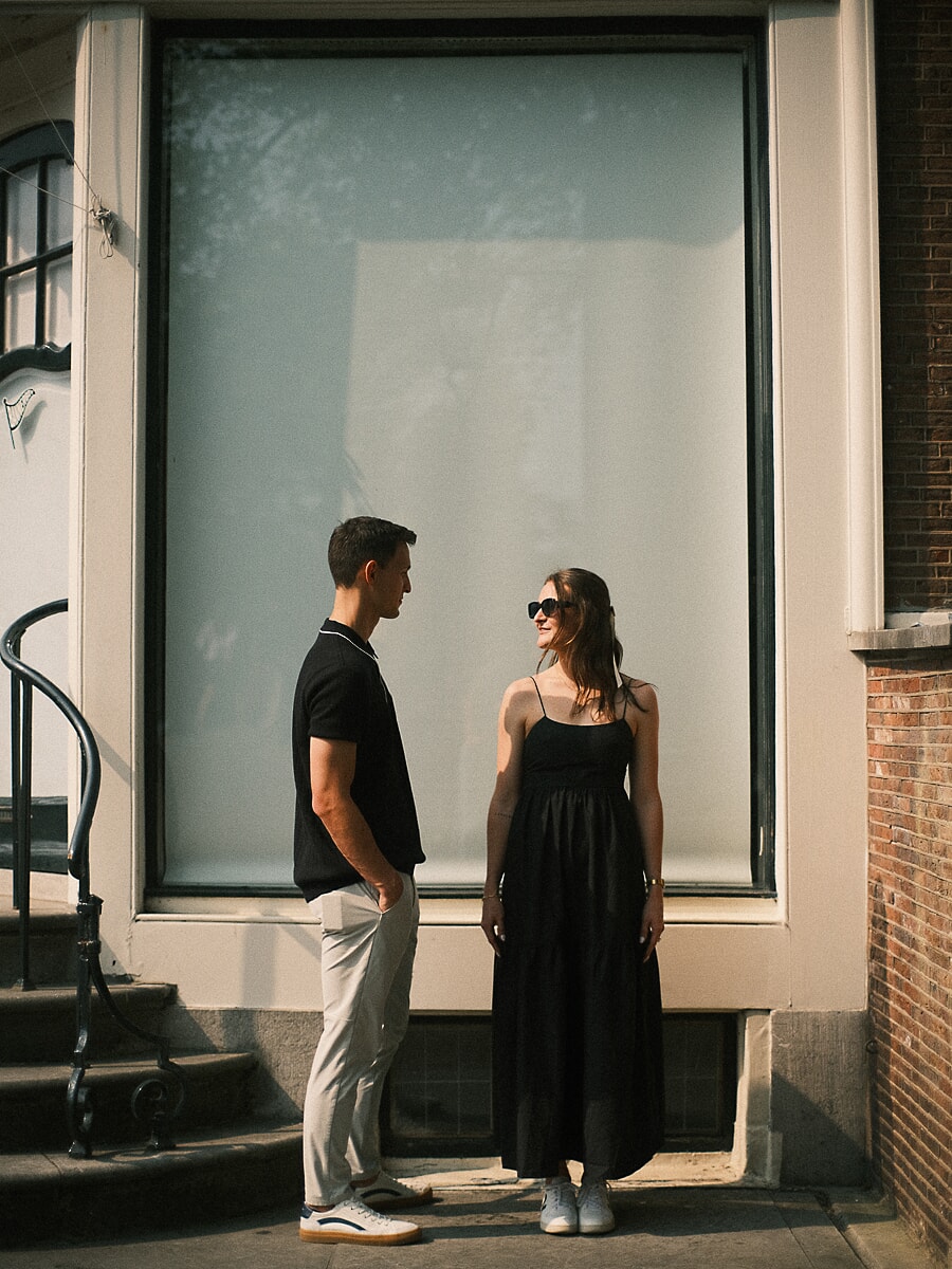 Engaged couple facing each other beside an Amsterdam shop window in hard afternoon light
