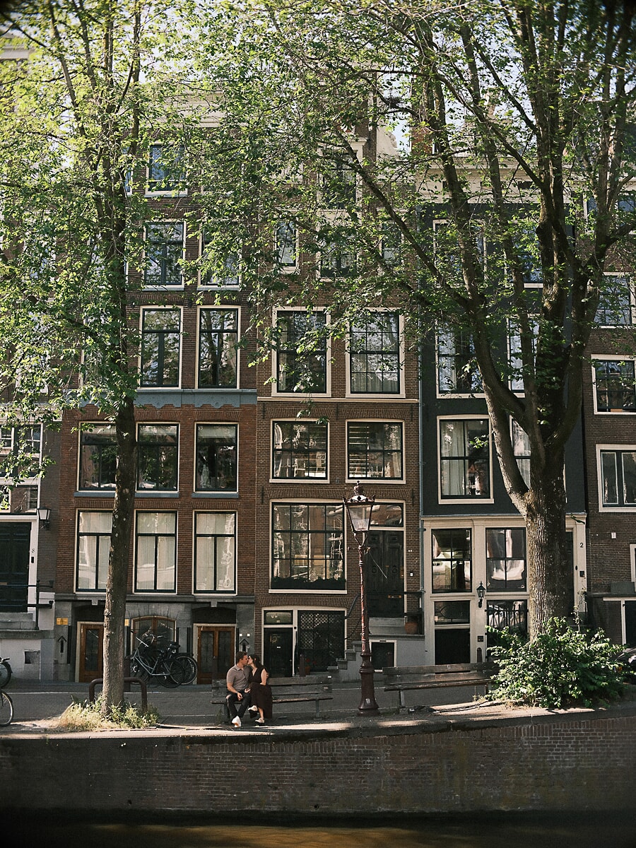 Engaged couple small against the tall canal houses of Amsterdam, a wide frame from their engagement shoot