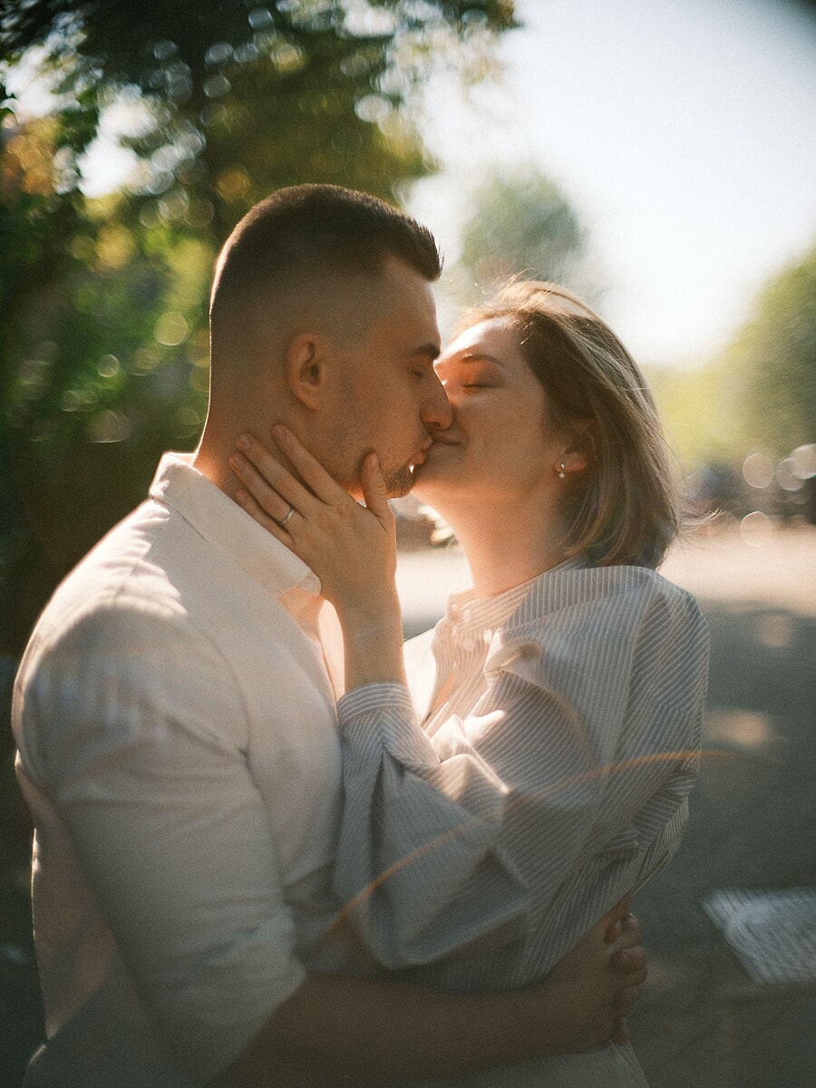 Engaged couple kissing in warm backlight, her engagement ring against his jaw during their engagement shoot in Amsterdam