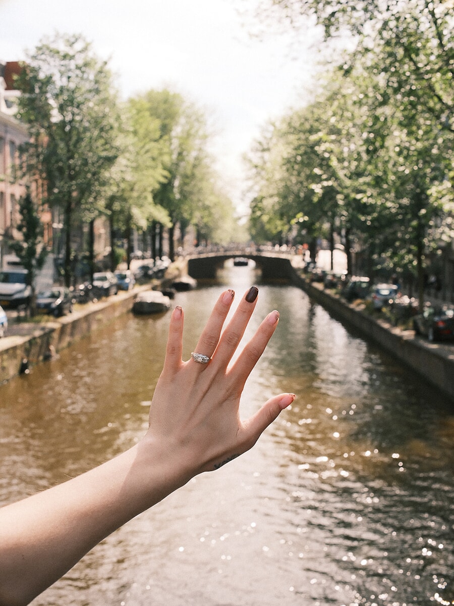 Engagement ring on a raised hand above a sunlit Amsterdam canal after the proposal