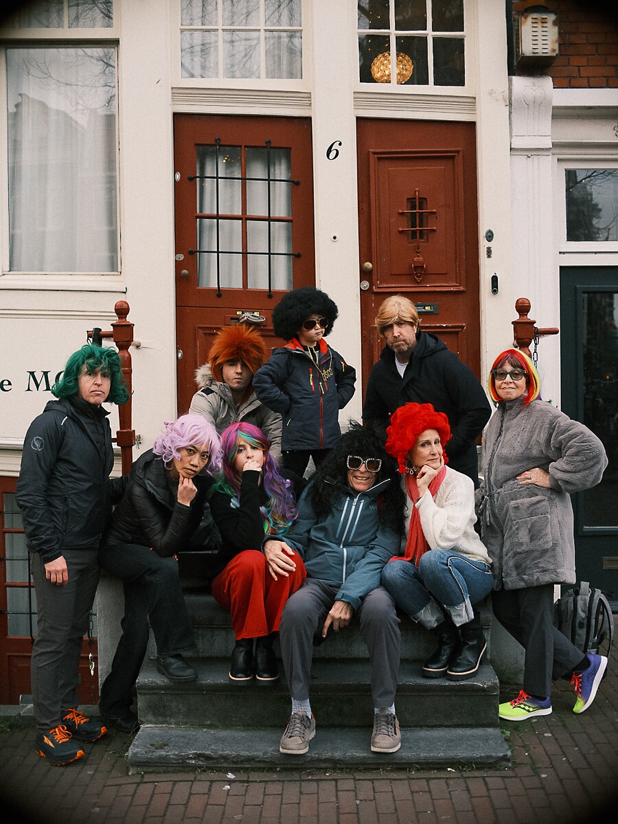 Family in bright wigs and sunglasses on the red front steps of an Amsterdam house, playing for the camera