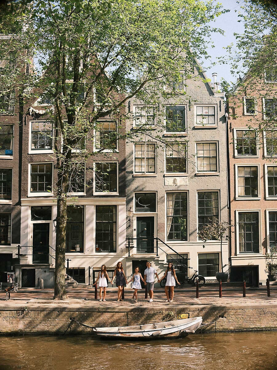 Hand in hand along the quay, a family of five dwarfed by the tall canal houses of Amsterdam