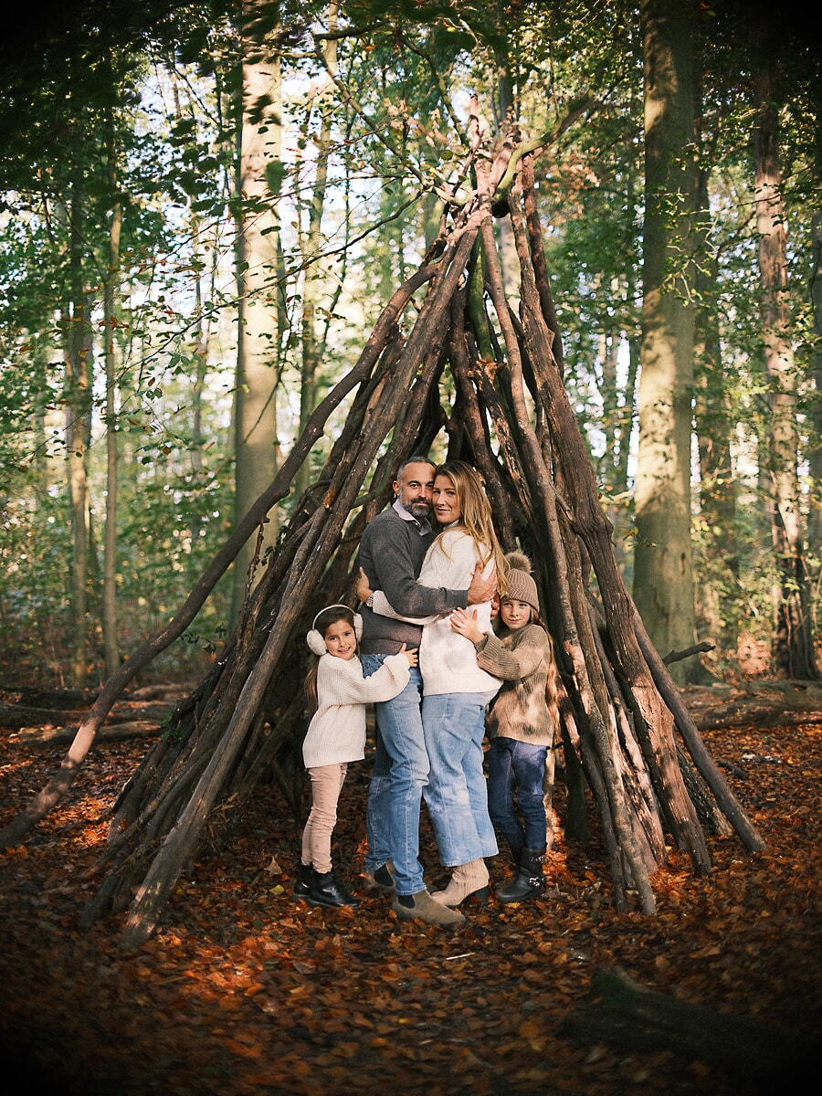 Parents and children holding each other inside a branch shelter in the woods, an autumn family photoshoot in Amsterdam