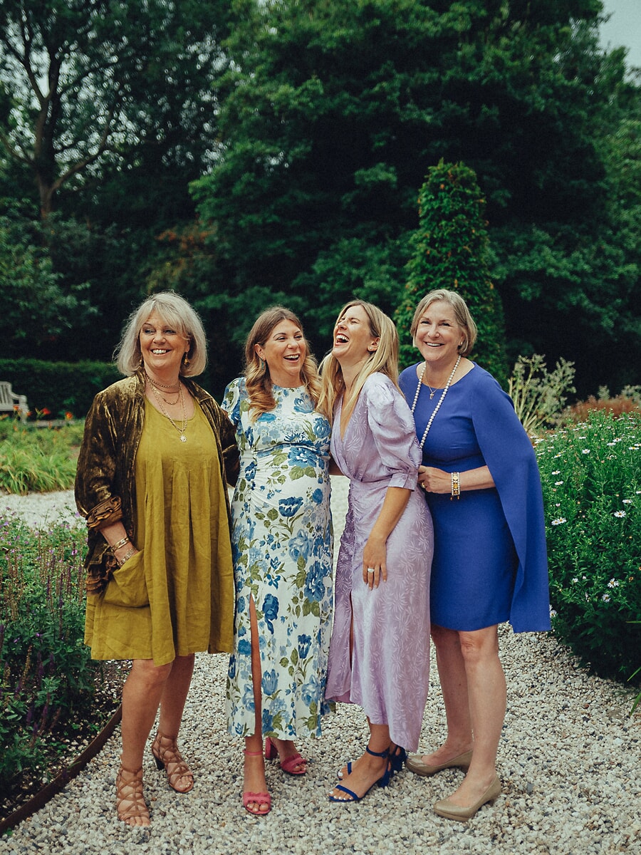 Four women from three generations laughing together on a garden path at a family anniversary
