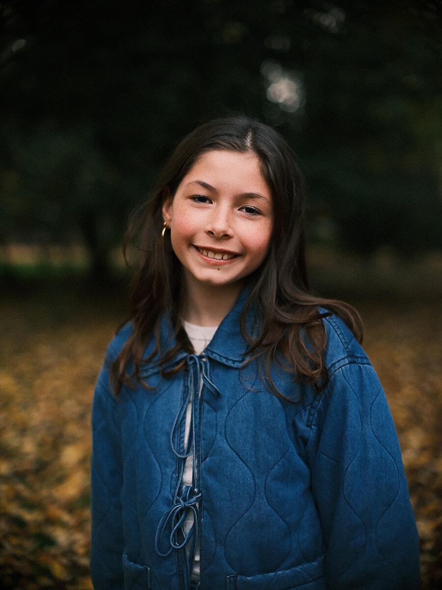Girl in a quilted denim jacket smiling in an Amsterdam park, a portrait session among golden leaves