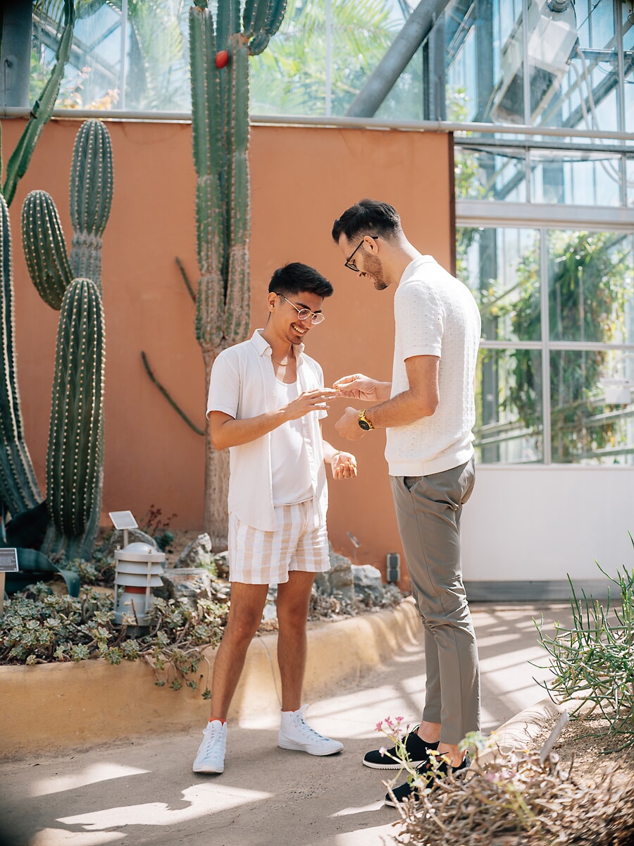 Two men exchanging a ring in the Hortus Botanicus greenhouse during their couple photoshoot in Amsterdam