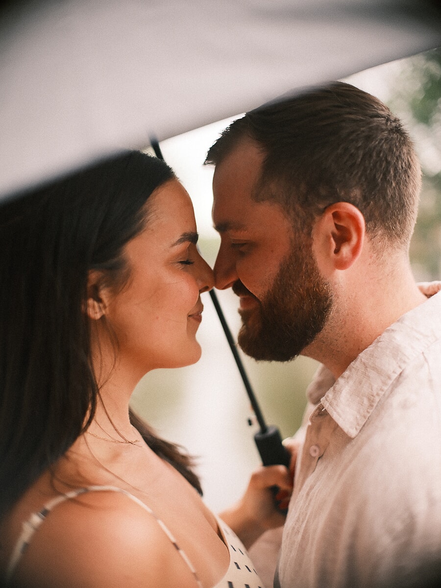 Couple nose to nose under an umbrella in the rain, an intimate portrait from their lovestory shoot in Amsterdam