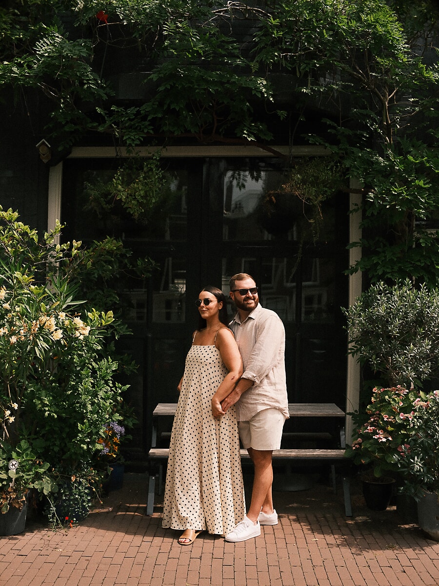 Couple leaning together under climbing greenery outside a dark Amsterdam facade, a relaxed loveshoot portrait
