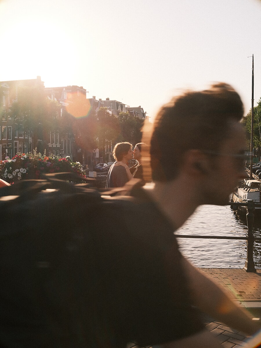 Two people kissing at sunset while a cyclist blurs past, documentary couple photography in Amsterdam
