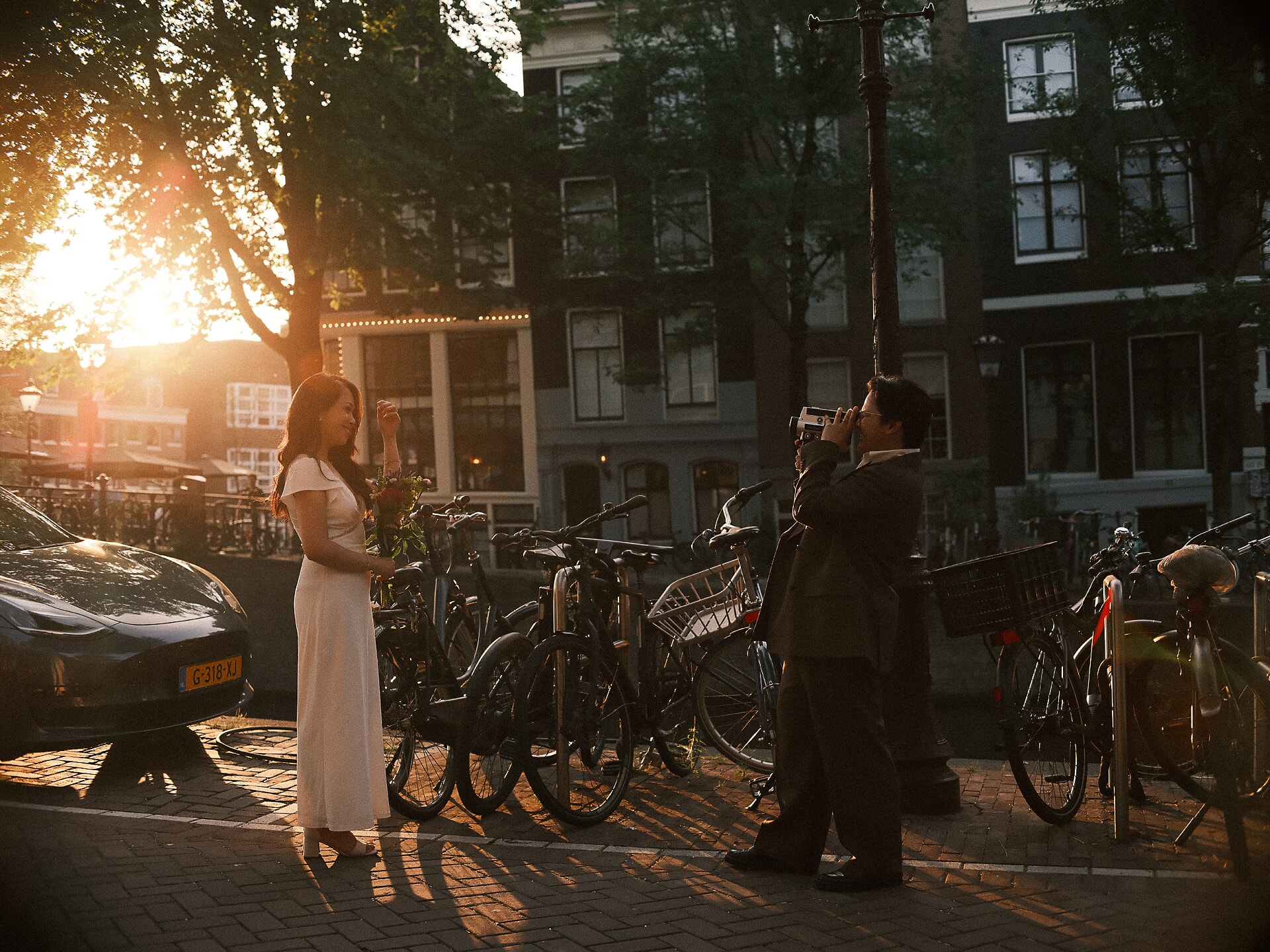 Newlyweds filming each other on a vintage cine camera by a canal at golden hour, a wedding shoot with a professional photographer in Amsterdam