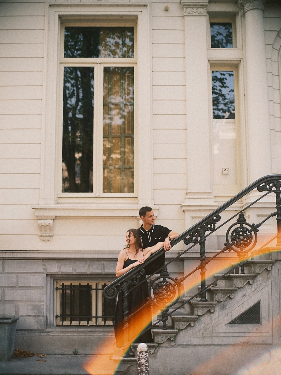 Couple on the ornate staircase of an Amsterdam canal house with cinematic flare across the frame, a pre-wedding portrait