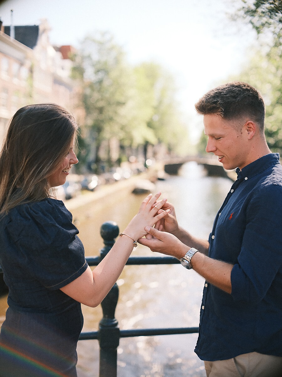 Man sliding the engagement ring onto her finger beside a bright Amsterdam canal, moments after the proposal
