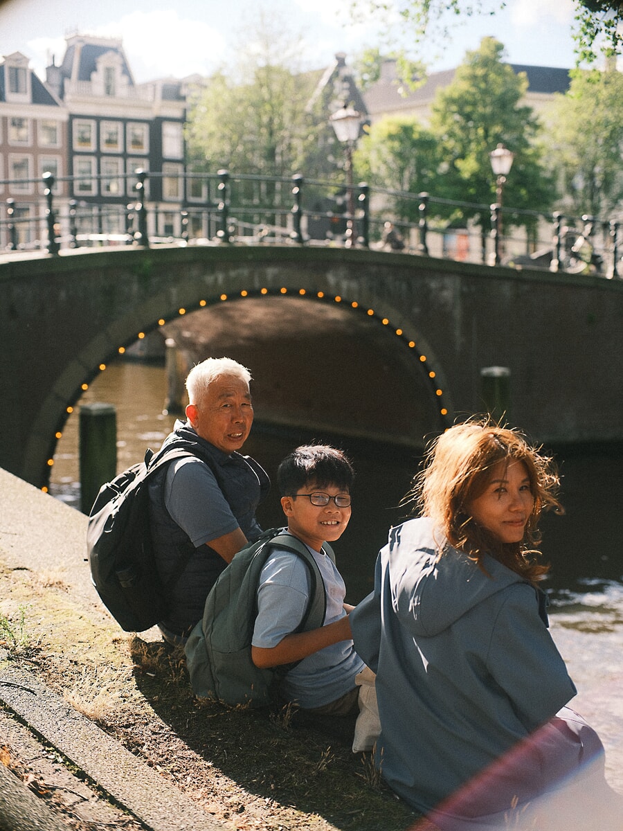 Three generations at the water's edge beneath a lit arched bridge, a storytelling family portrait in Amsterdam