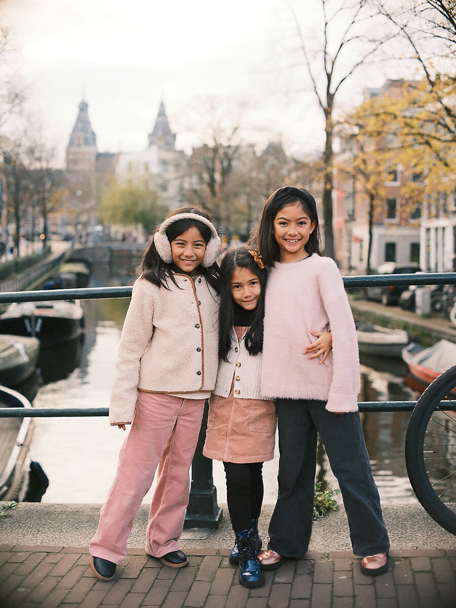 Three sisters leaning on an Amsterdam canal railing, a candid frame from a family portrait session