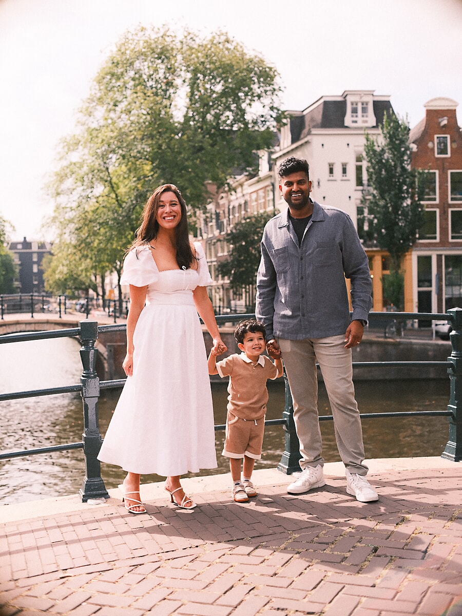 Parents holding their toddler's hands on an Amsterdam canal bridge, an unstaged shot from their family shoot