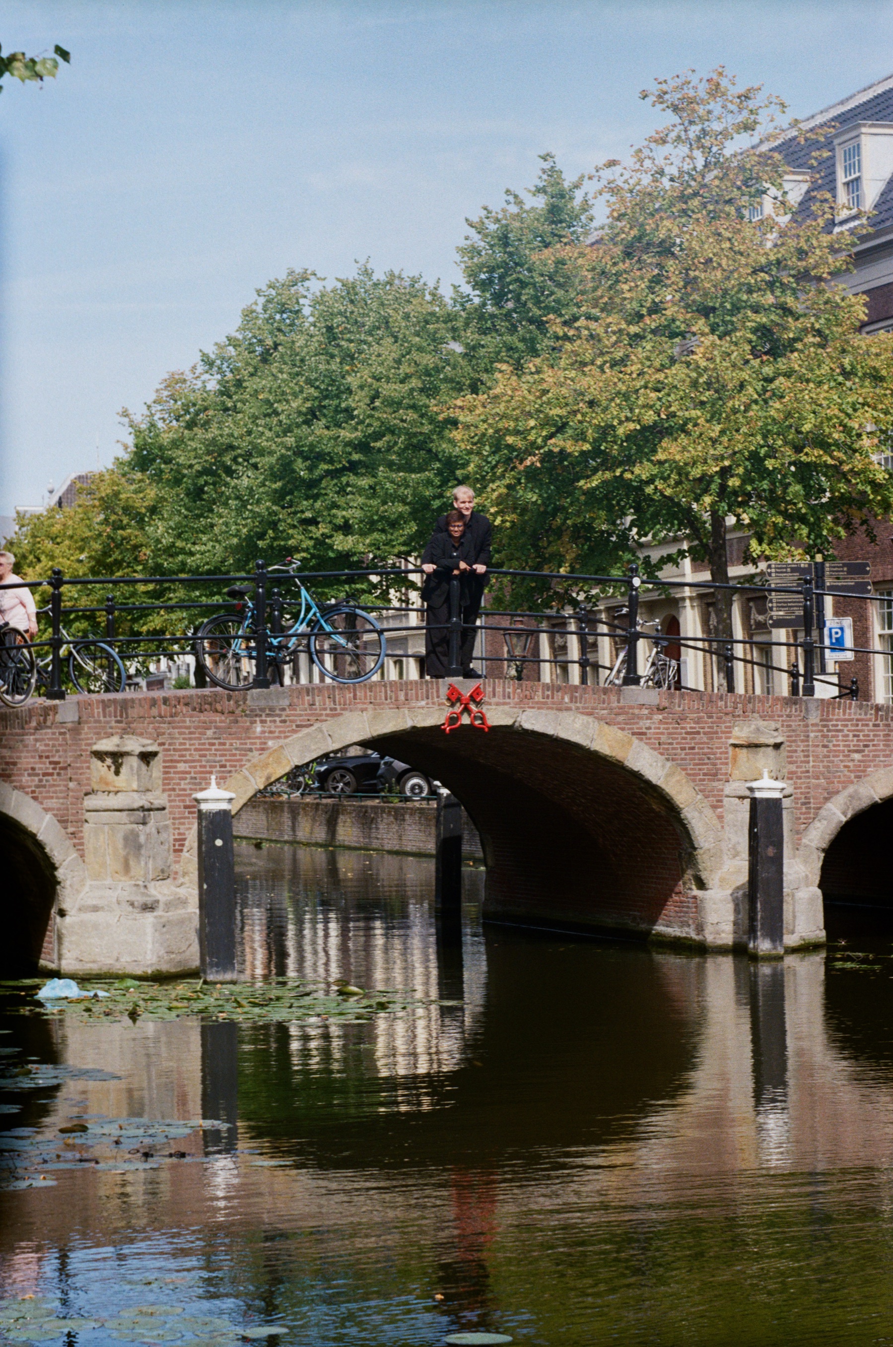 Arched stone bridge over a canal in Leiden, a figure in black at the railing and the arches mirrored in the still water