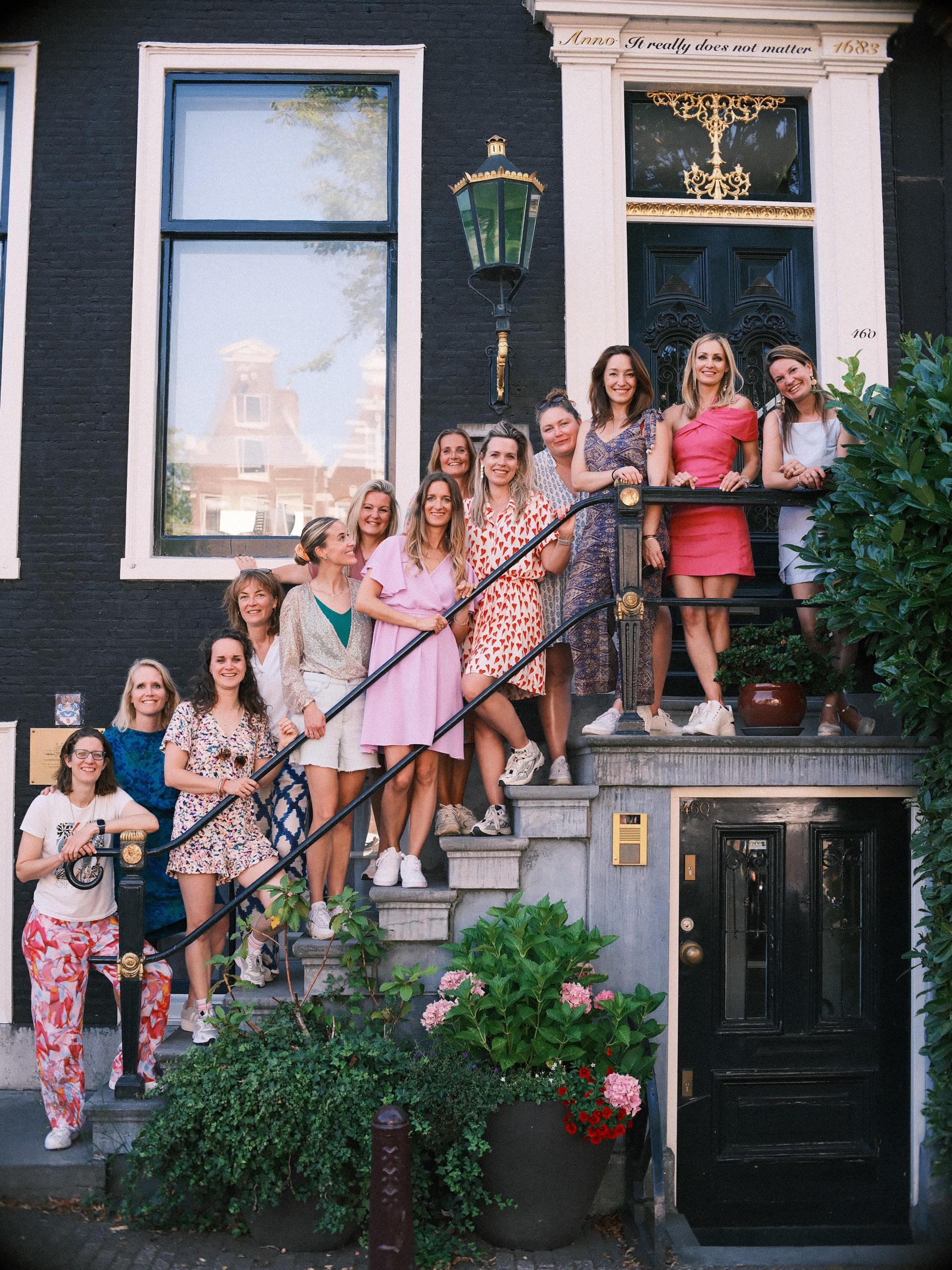 The whole bachelorette with twelve friends on the stone stoop of a dark canal house, waving under a green lantern