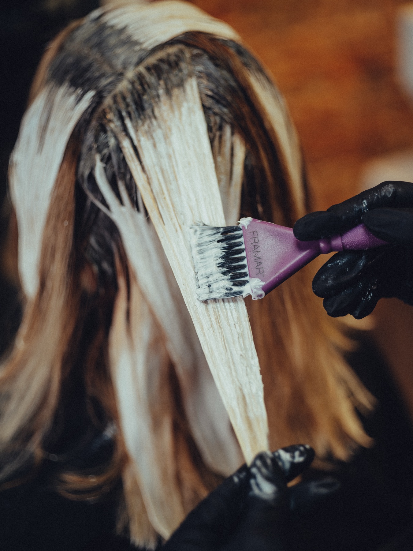 Handen in zwarte handschoenen brengen met een paarse kwast ontkleuring aan op lange lokken haar, tijdens een balayage