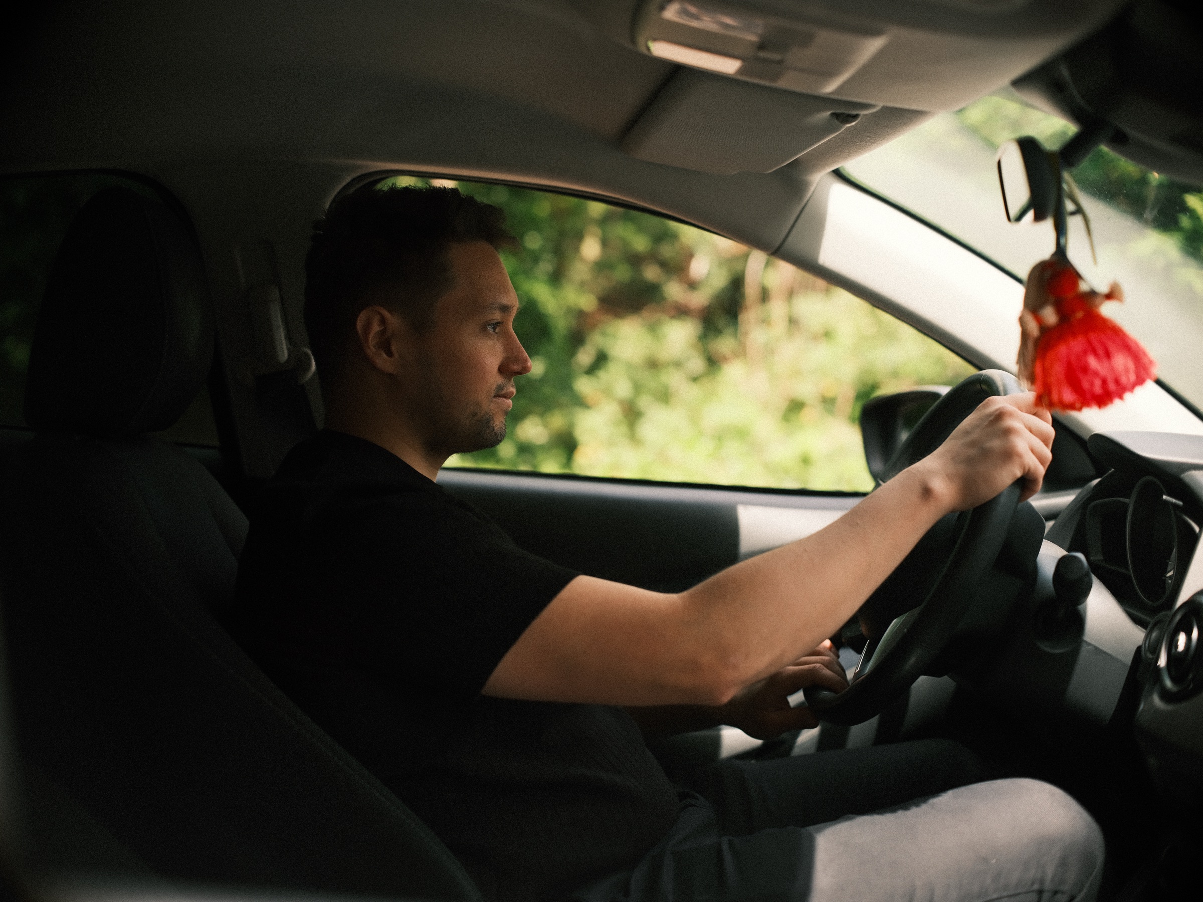 Profiel van de man achter het stuur van zijn auto, met een rood kwastje aan de spiegel, het laatste beeld van zijn fotoshoot