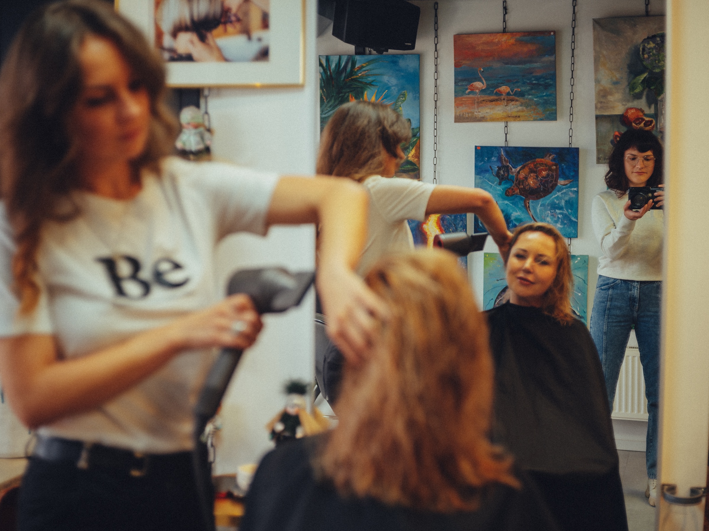 Kapster föhnt het haar van een klant voor een spiegel met schilderijen van flamingo's en een schildpad in de beautystudio