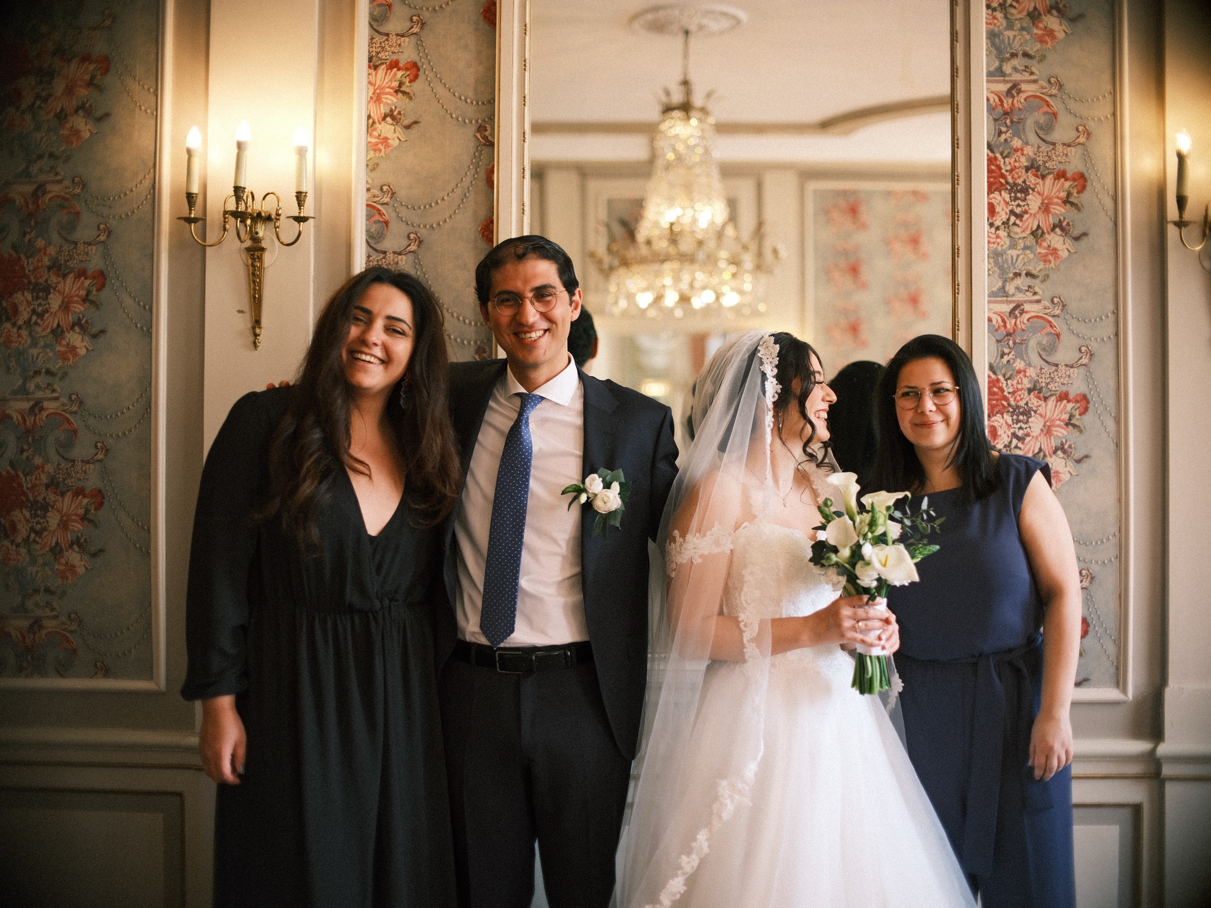 Bruid en bruidegom met twee vriendinnen voor een vergulde spiegel en bloemenbehang, aan het eind van hun kasteelbruiloft