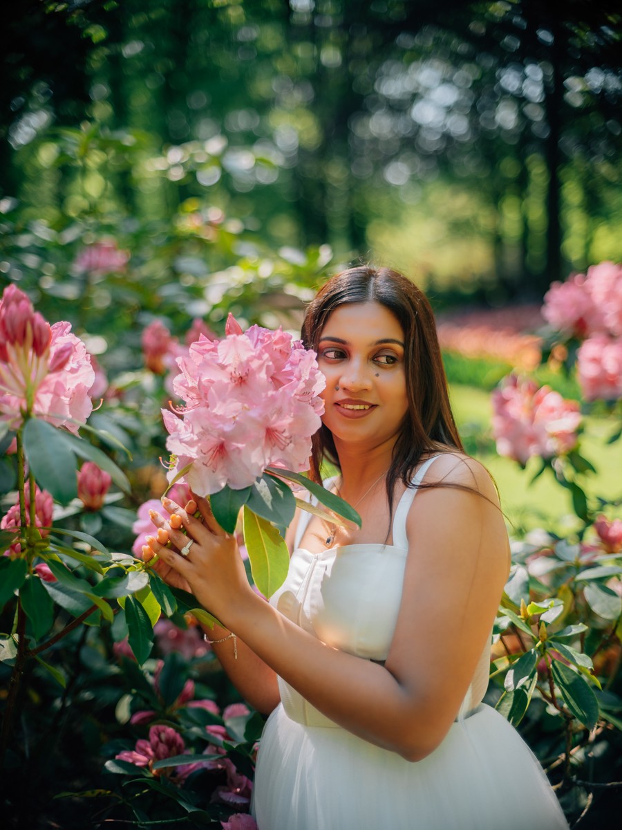 Bruid houdt roze rododendronbloemen bij haar gezicht, terwijl haar ring en oranje nagels het zonlicht vangen