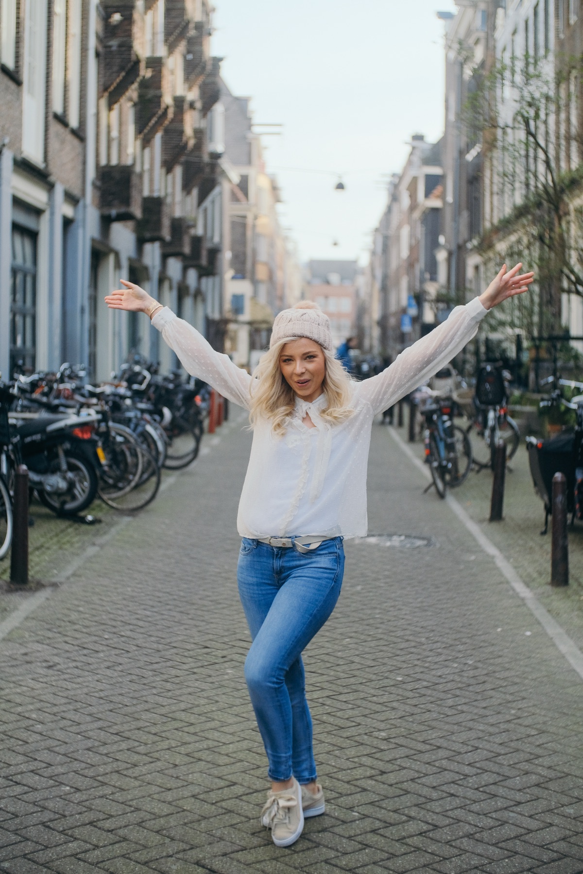 Bride-to-be throwing her arms wide in an empty side street, rows of parked bikes and tall brick houses on both sides