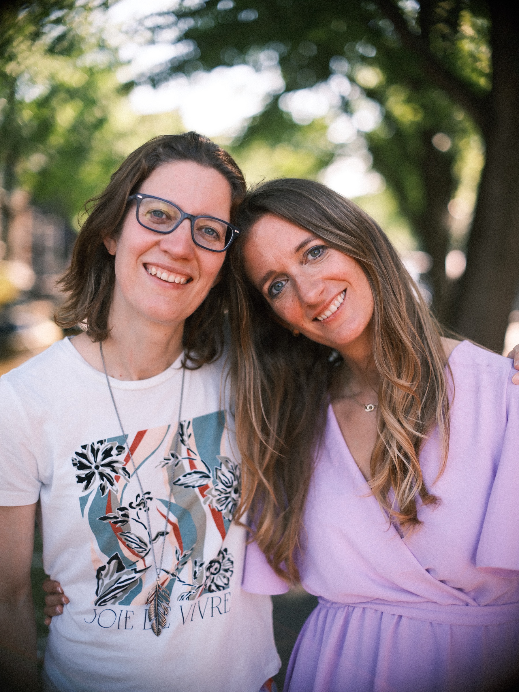 Bride-to-be cheek to cheek with a friend in glasses and a printed T-shirt, the canal blurred behind them at her bachelorette