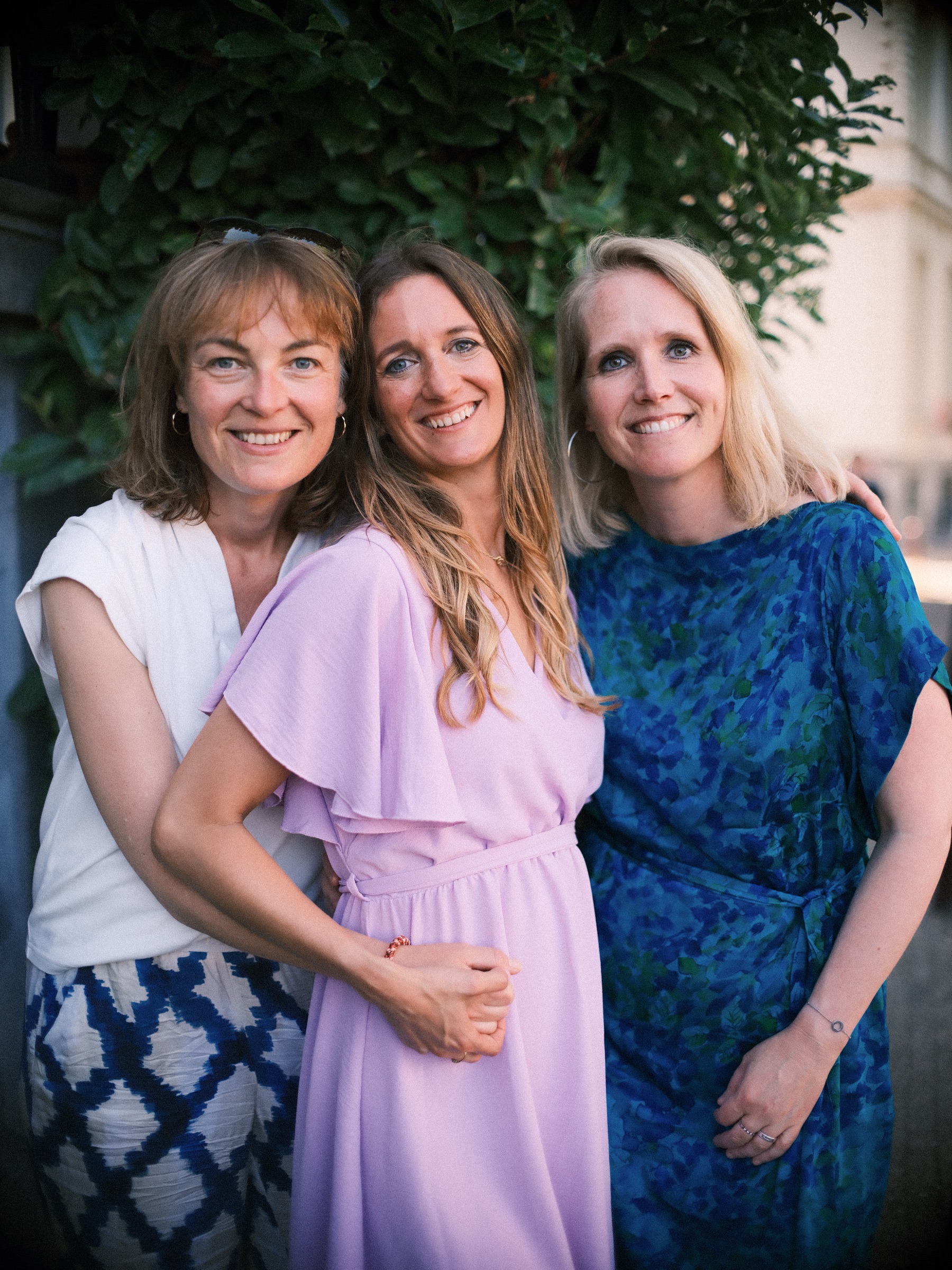Bride-to-be between two friends by a doorway framed in ivy at her bachelorette, one in a vivid blue dress