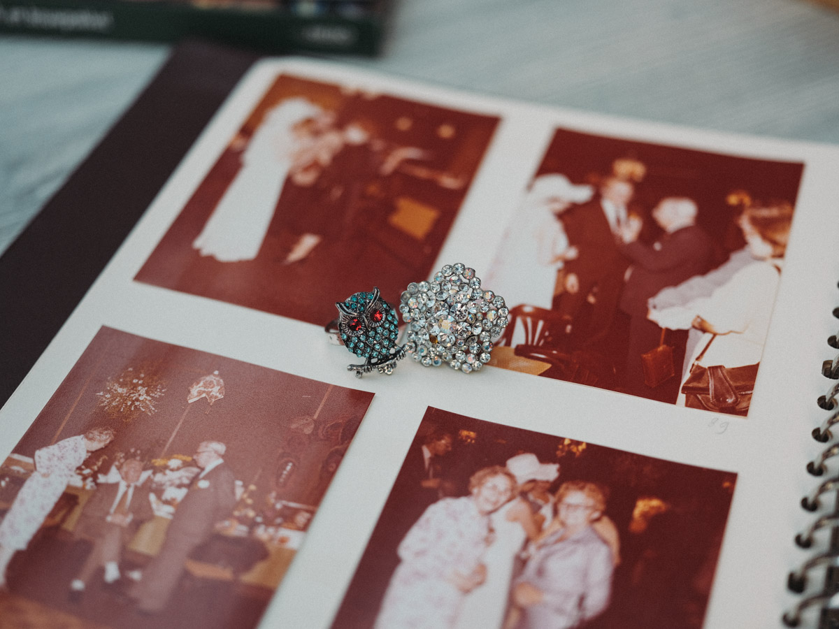 Two brooches, an owl with red eyes and a round one full of rhinestones, lying on an album of the couple’s wedding photos