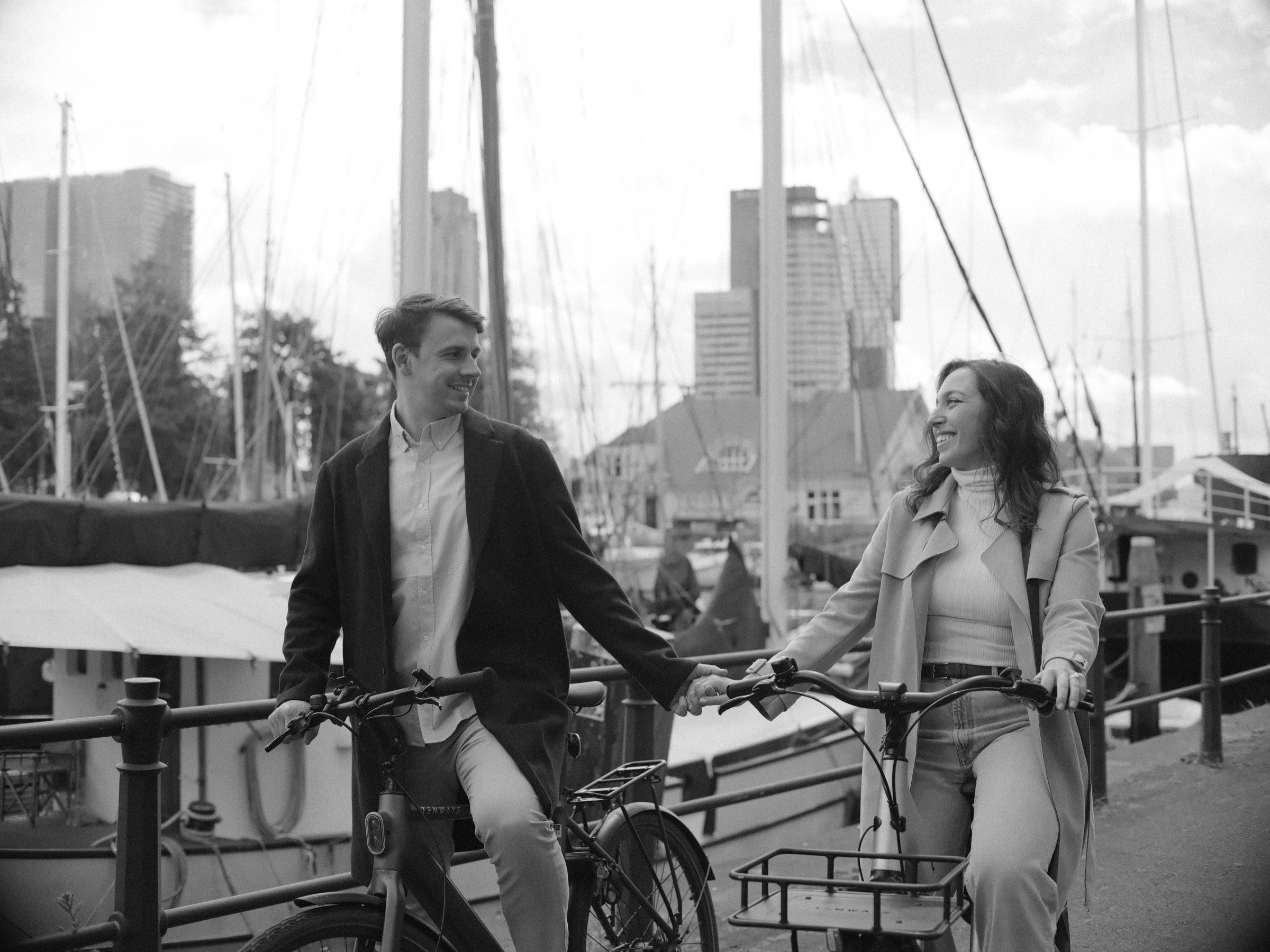 Couple on two city bikes by the masts of the Veerhaven in black and white, an engagement shoot in the Scheepvaartkwartier