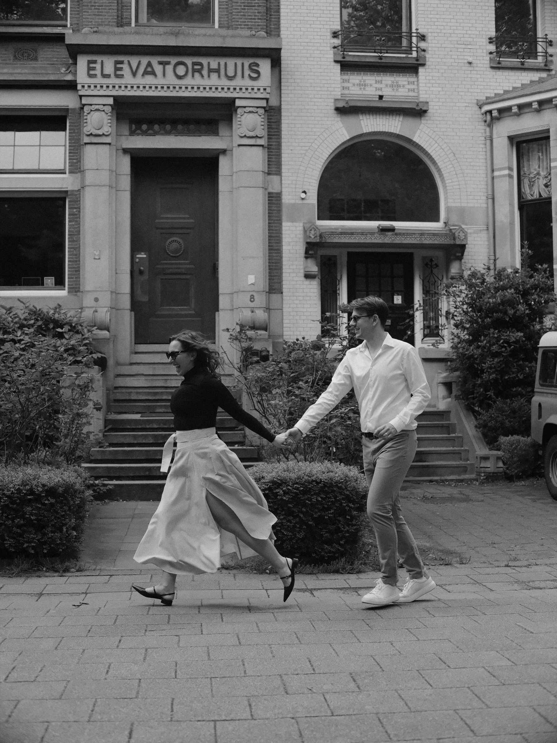 Running hand in hand past the Elevatorhuis on the Parklaan in black and white, her pleated skirt flying out behind her